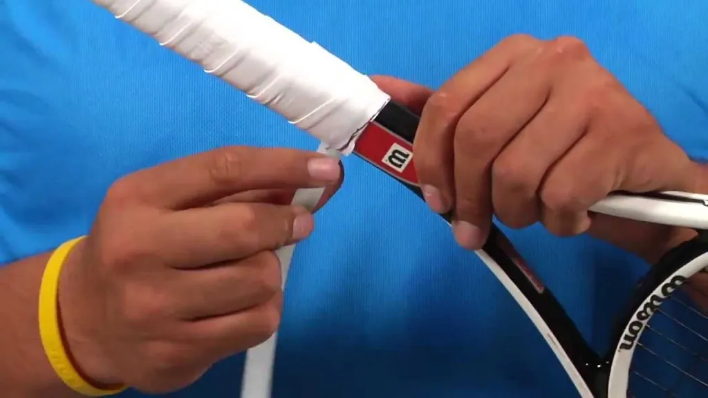 Close-up of hands applying an overgrip to a tennis racket handle
