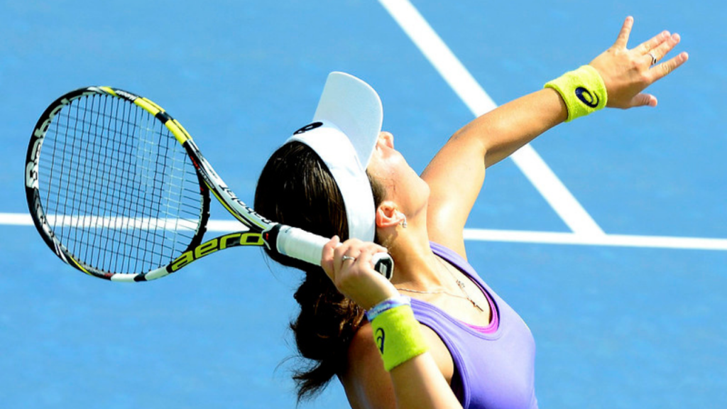 here two professional players play tennis on a blue hard court. one player is in the process of serving with a babolat racket